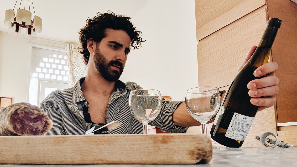 A stressed out guy looks at a bottle of wine and eats in a fancy kitchen