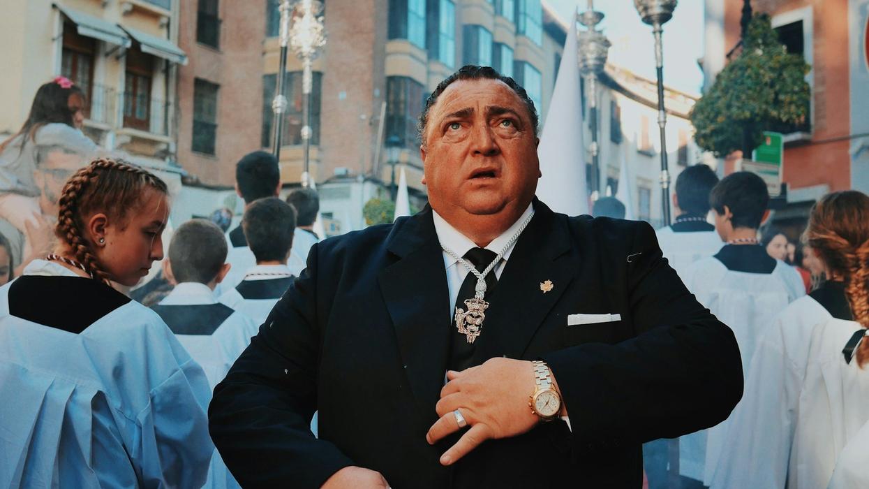 A stressed out man in a tuxedo looks to the sky as many young altar boys and girls walk around him.