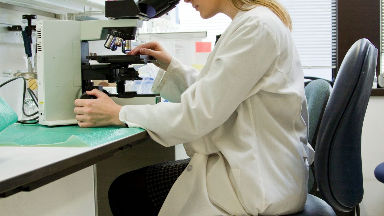 A woman in a white lab coat looking into a microscope