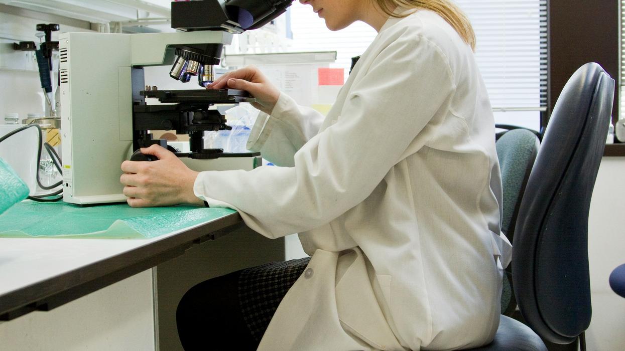 A woman in a white lab coat looking into a microscope