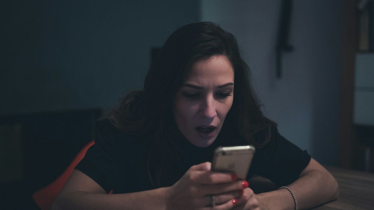 A woman looks into her cellphone with complete shock.