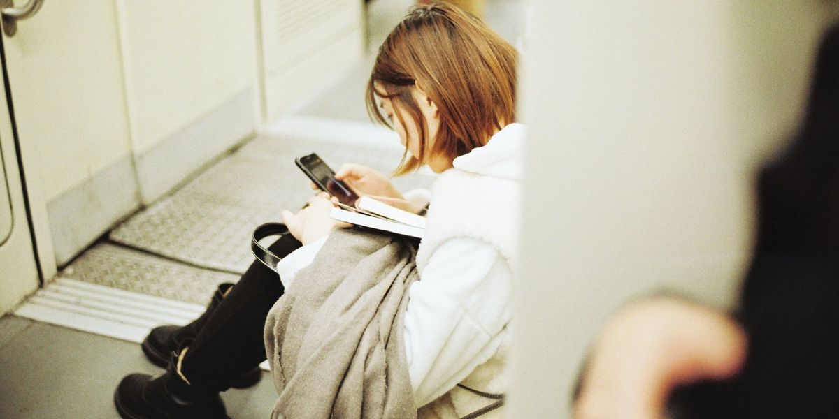 A woman sits on the floor of a train reading from her phone
