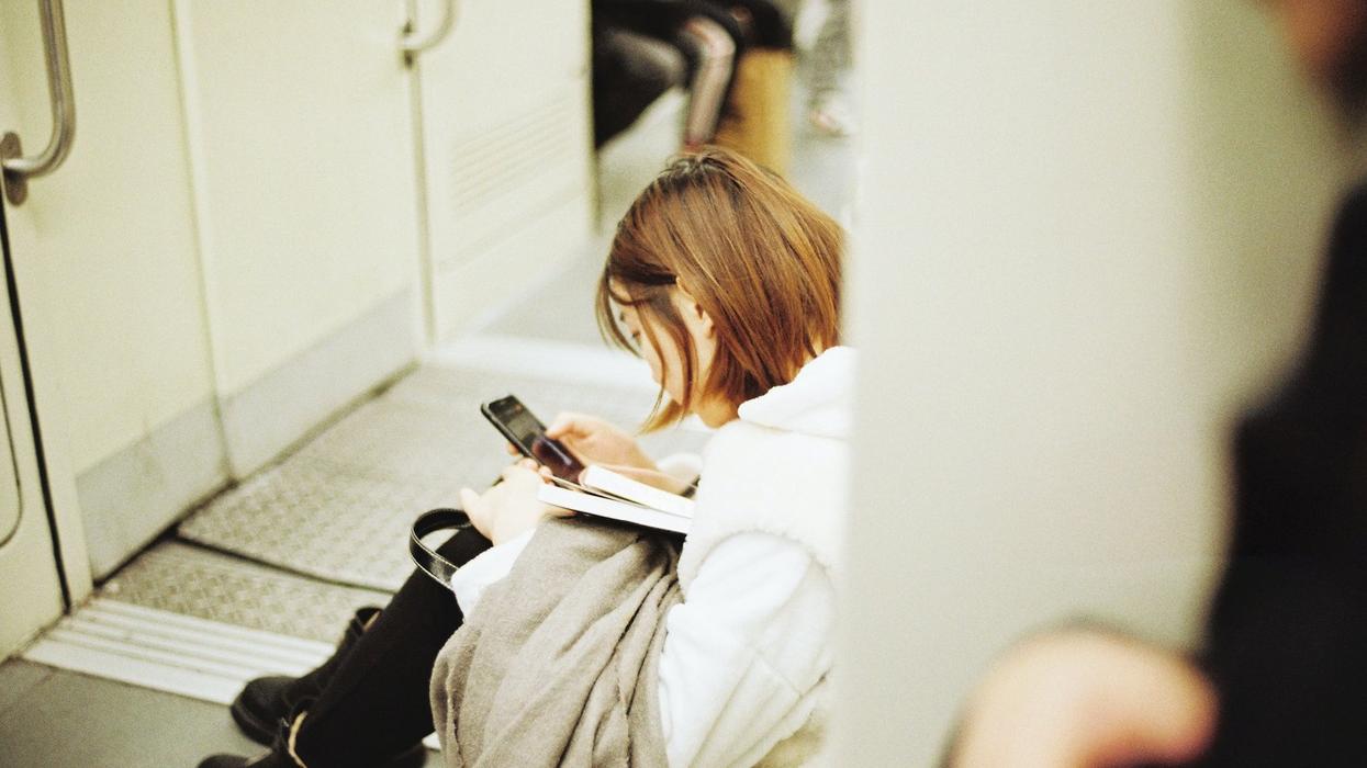 A woman sits on the floor of a train reading from her phone