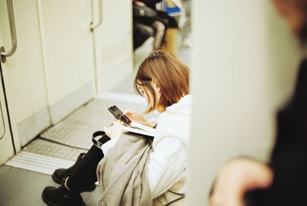 A woman sits on the floor of a train reading from her phone