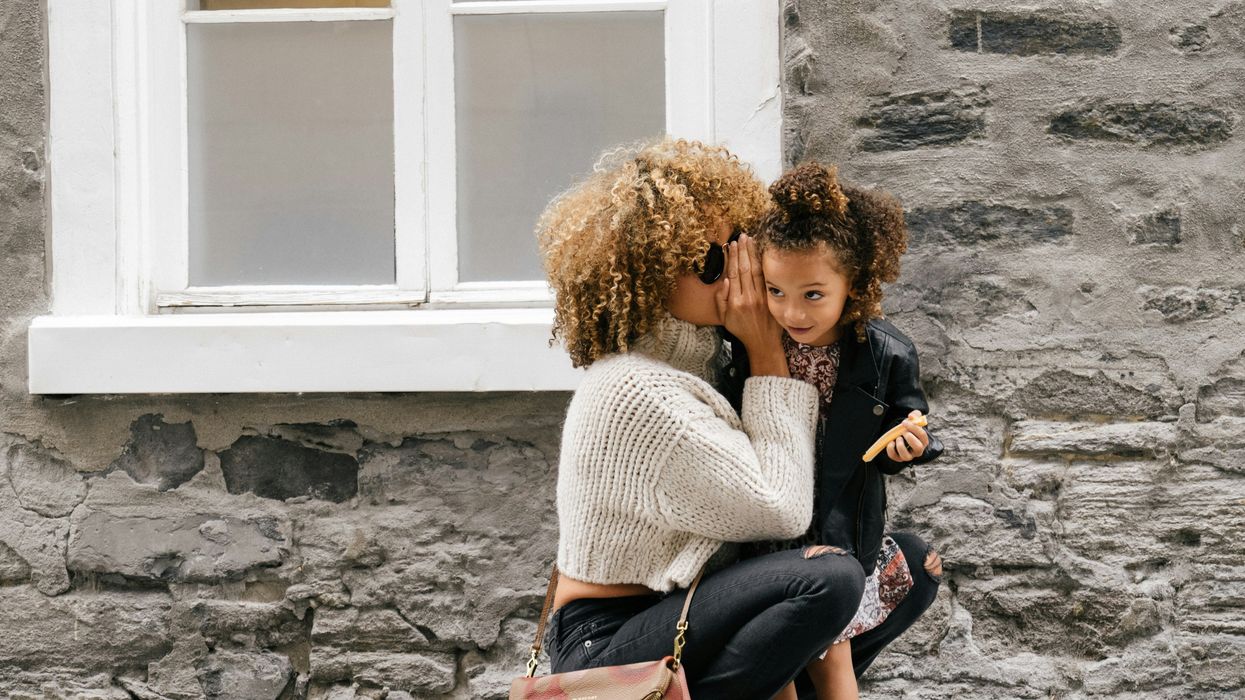 A woman whispering into her child's ear.