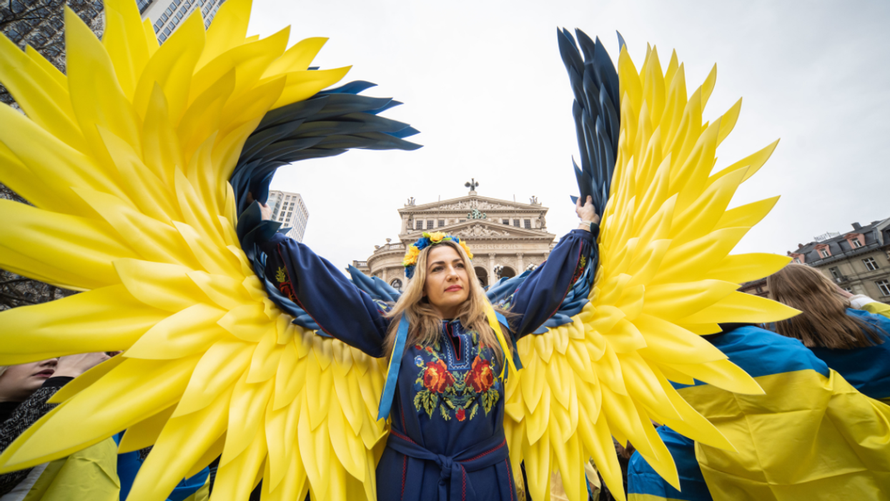 A woman with angel wings in Ukrainian colors stands in front of the Old Opera House.