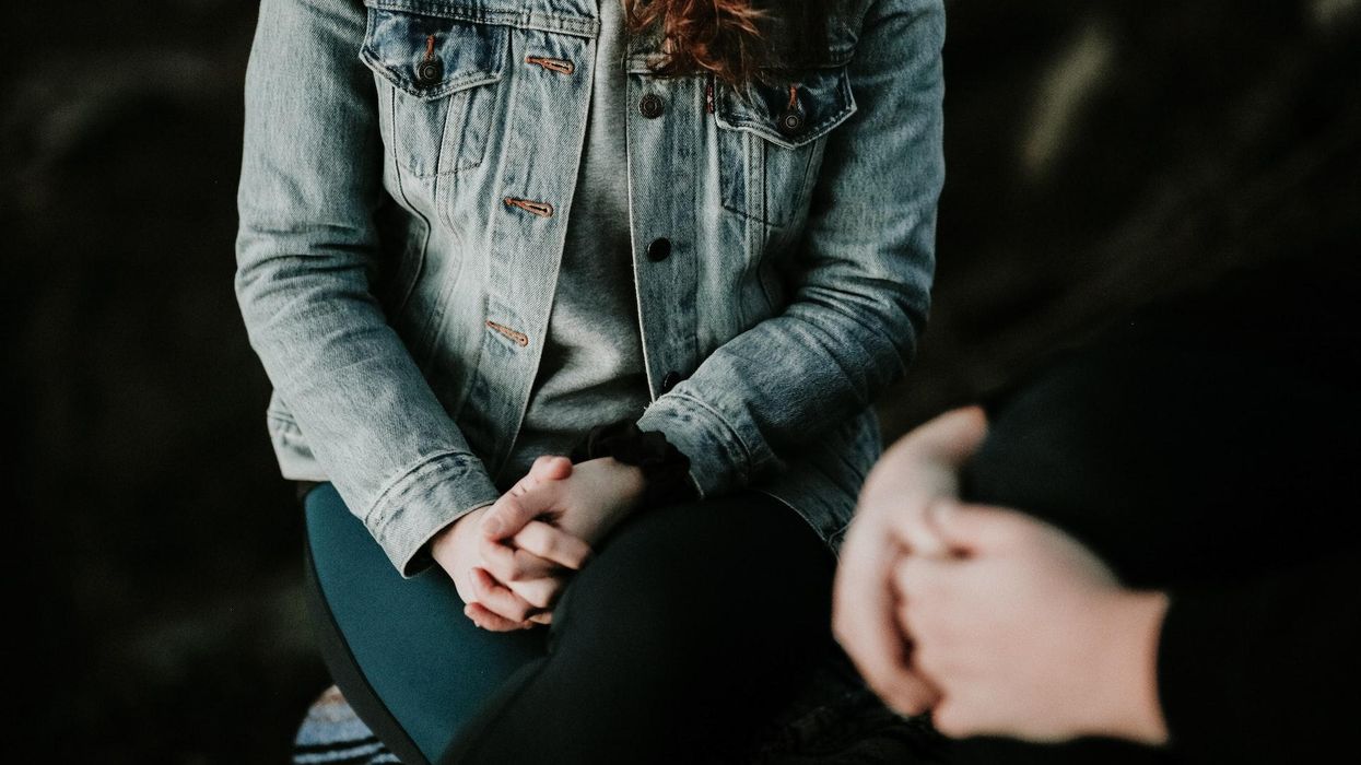 A woman with clasps hands sits across from her therapist