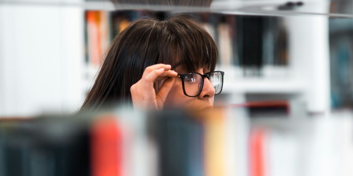 A woman with glasses peaking over a bookshelf