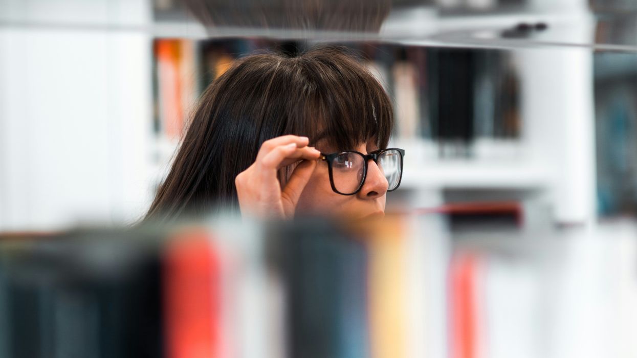 A woman with glasses peaking over a bookshelf