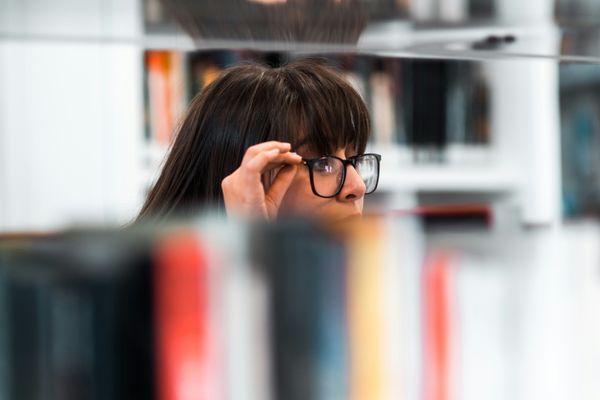 A woman with glasses peaking over a bookshelf