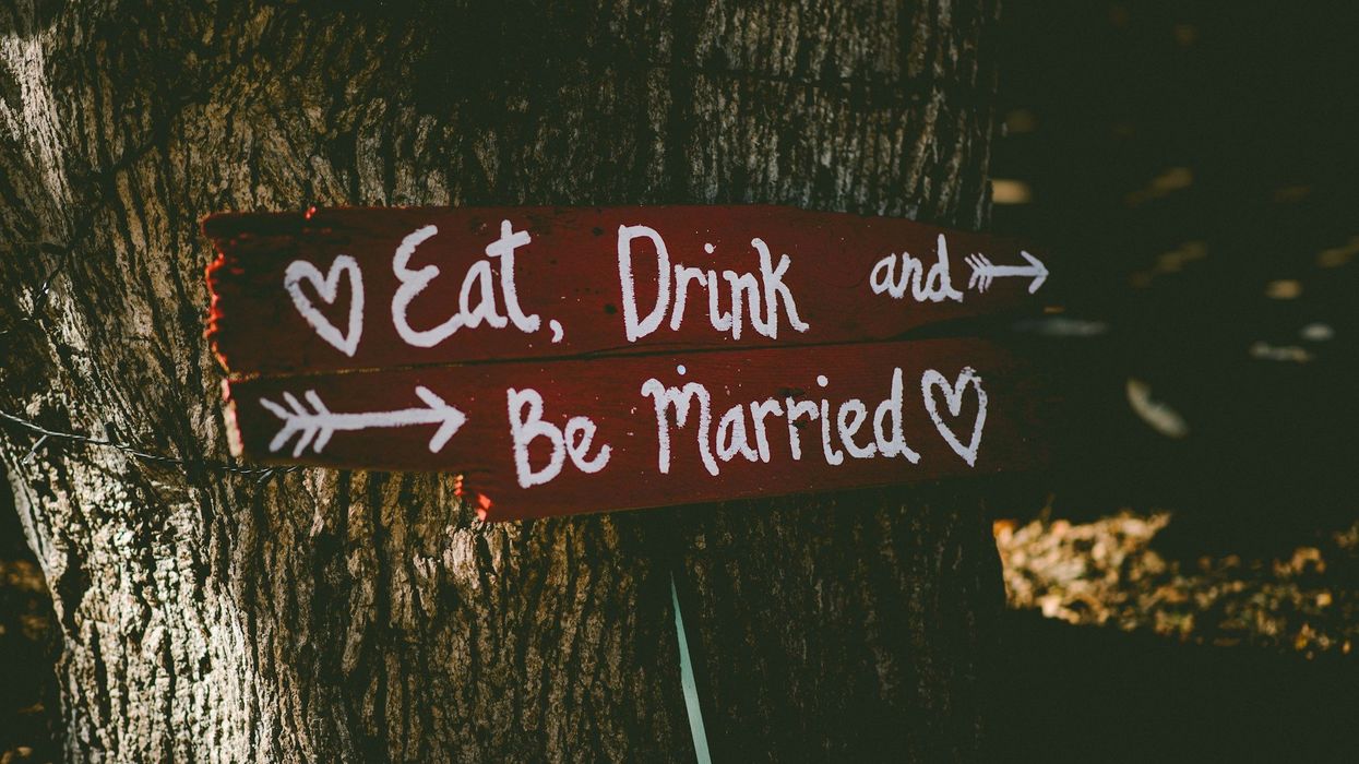 A wooden red sign that says "Eat, Drink and Be Married" is nailed to a tree.