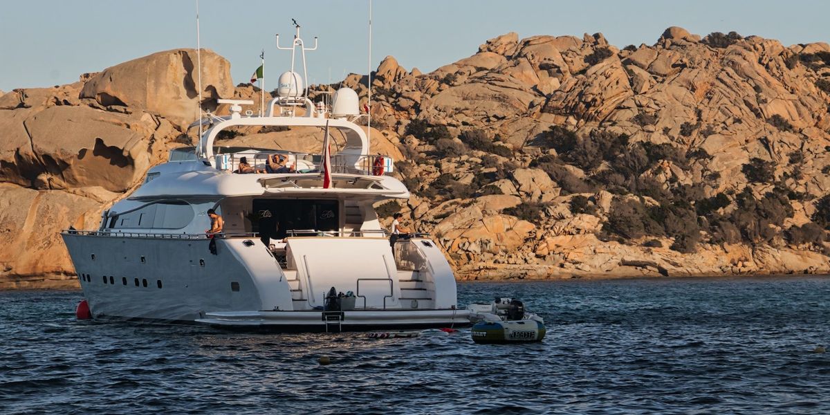 A yacht sits on water against a background of rocks as people luxuriate