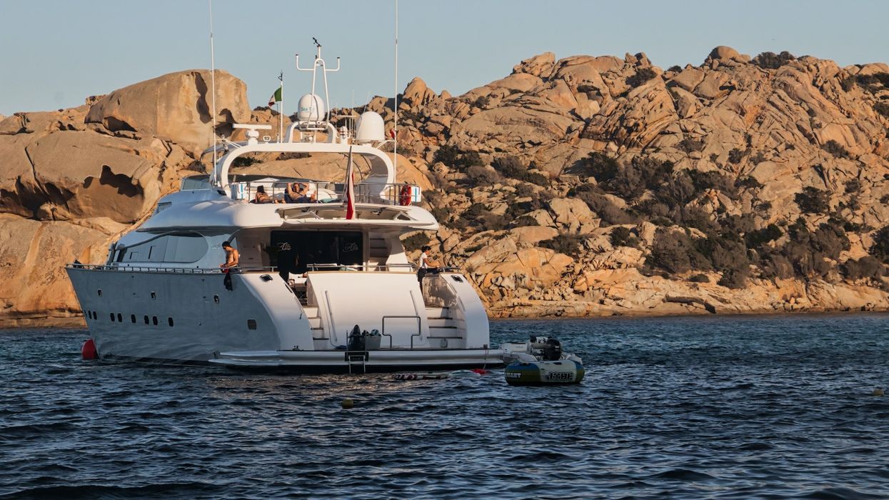 A yacht sits on water against a background of rocks as people luxuriate
