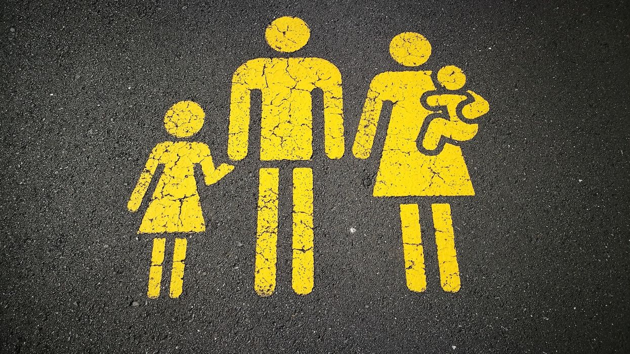 A yellow stick figure family painting (little girl, dad, mom, baby) on asphalt