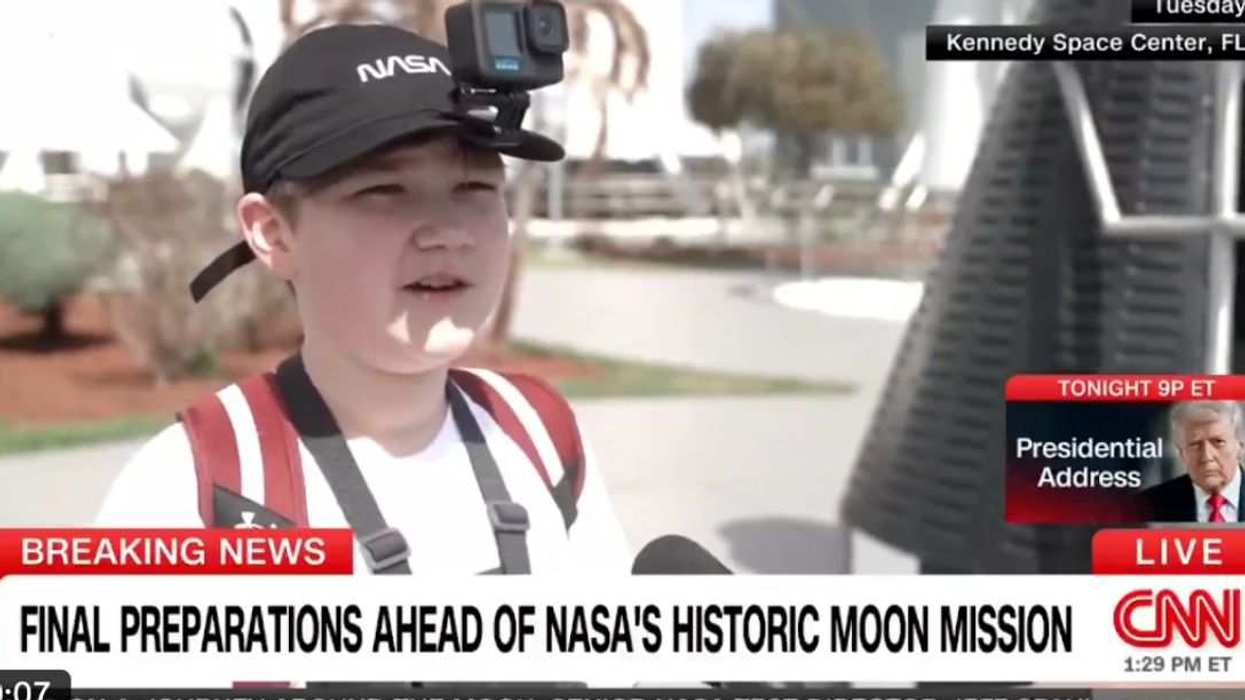A young attendee wearing a NASA cap with a mounted GoPro is interviewed by CNN at Kennedy Space Center ahead of the Artemis II launch.
