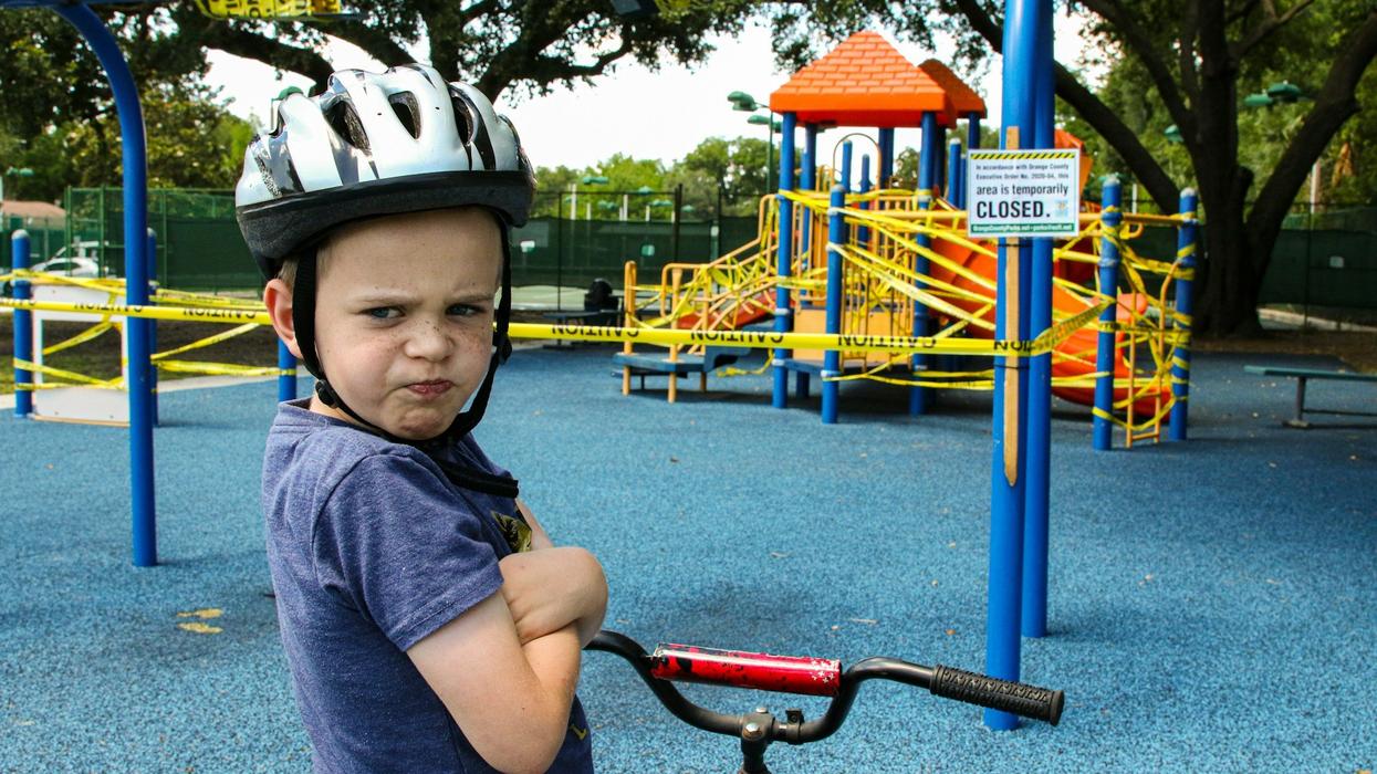 A young boy wearing a helmet, sitting on a bike, is angry the playground is closed.