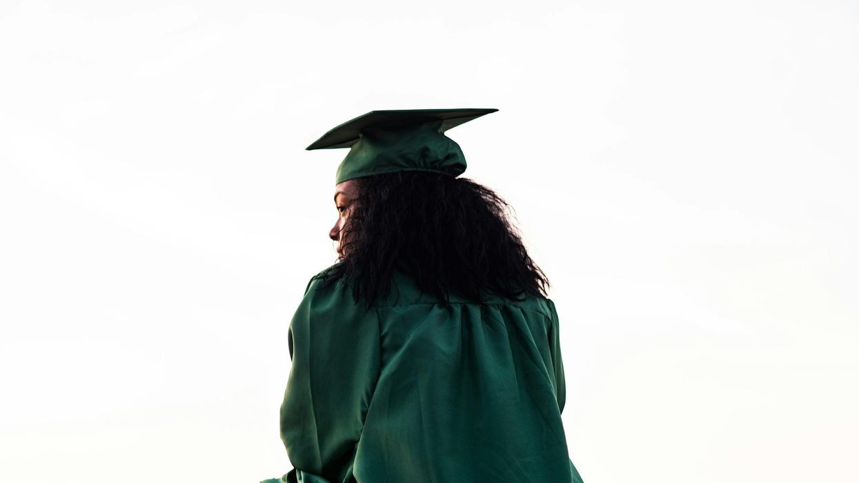 A young female graduate, in a green cap and gown, looks out into the unknown.