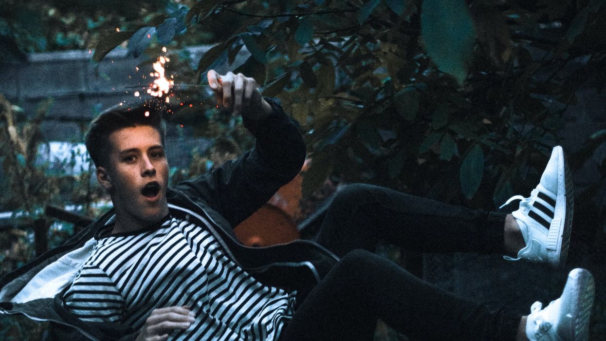 A young man bounces backwards on a trampoline while holding a lit sparkler