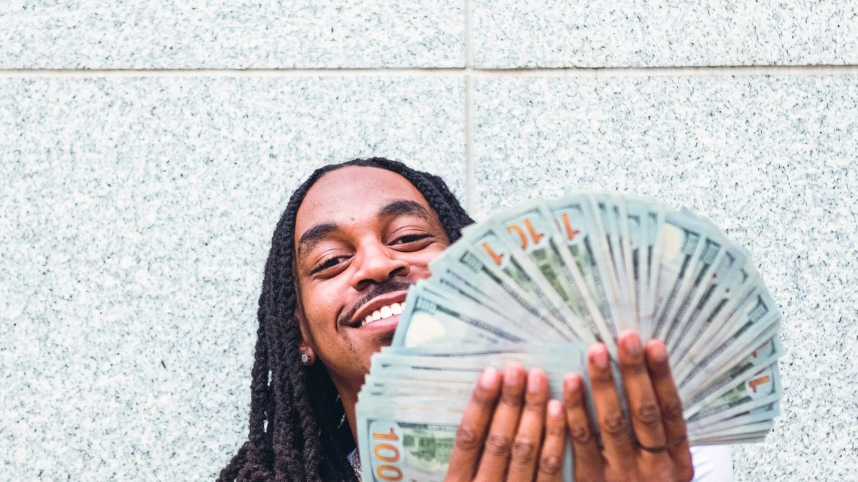 A young man displays a handful of hundred dollar bills.