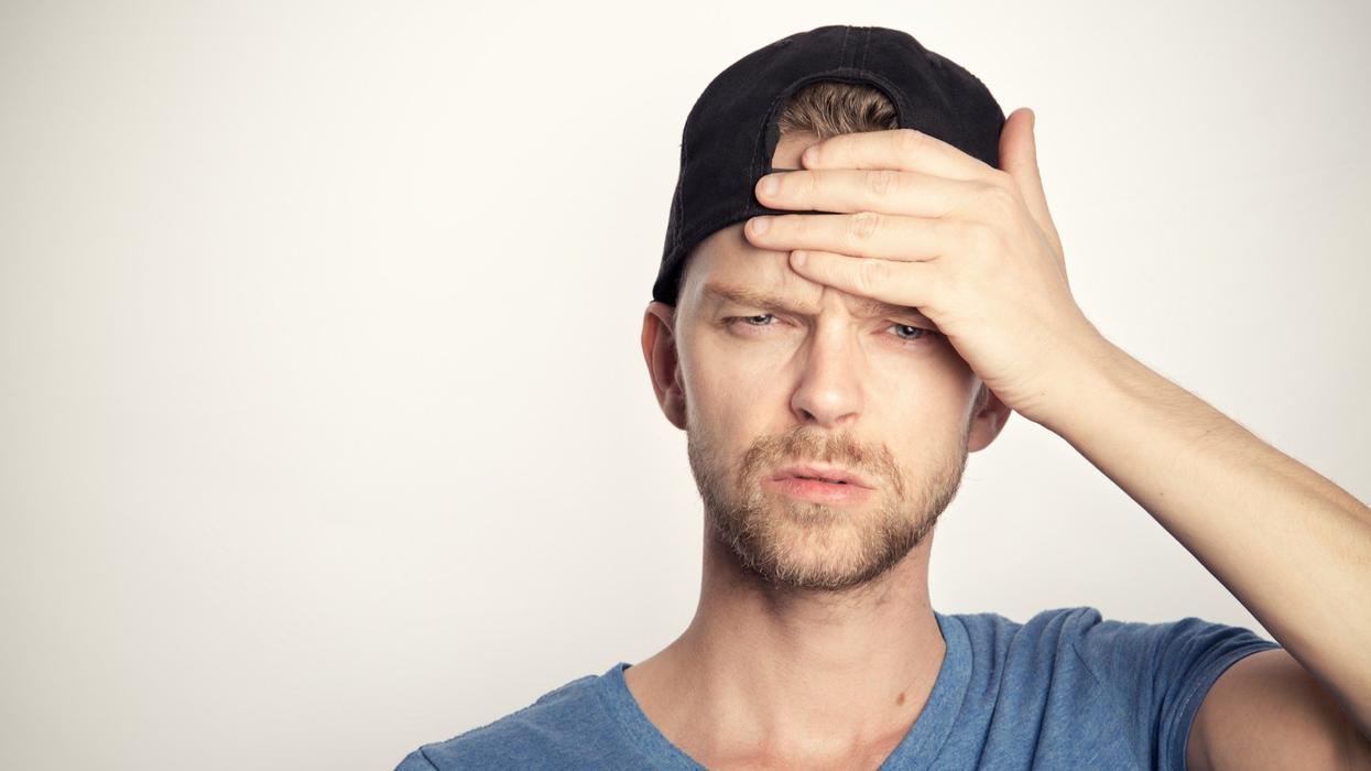 A young man holds his forehead in confusion