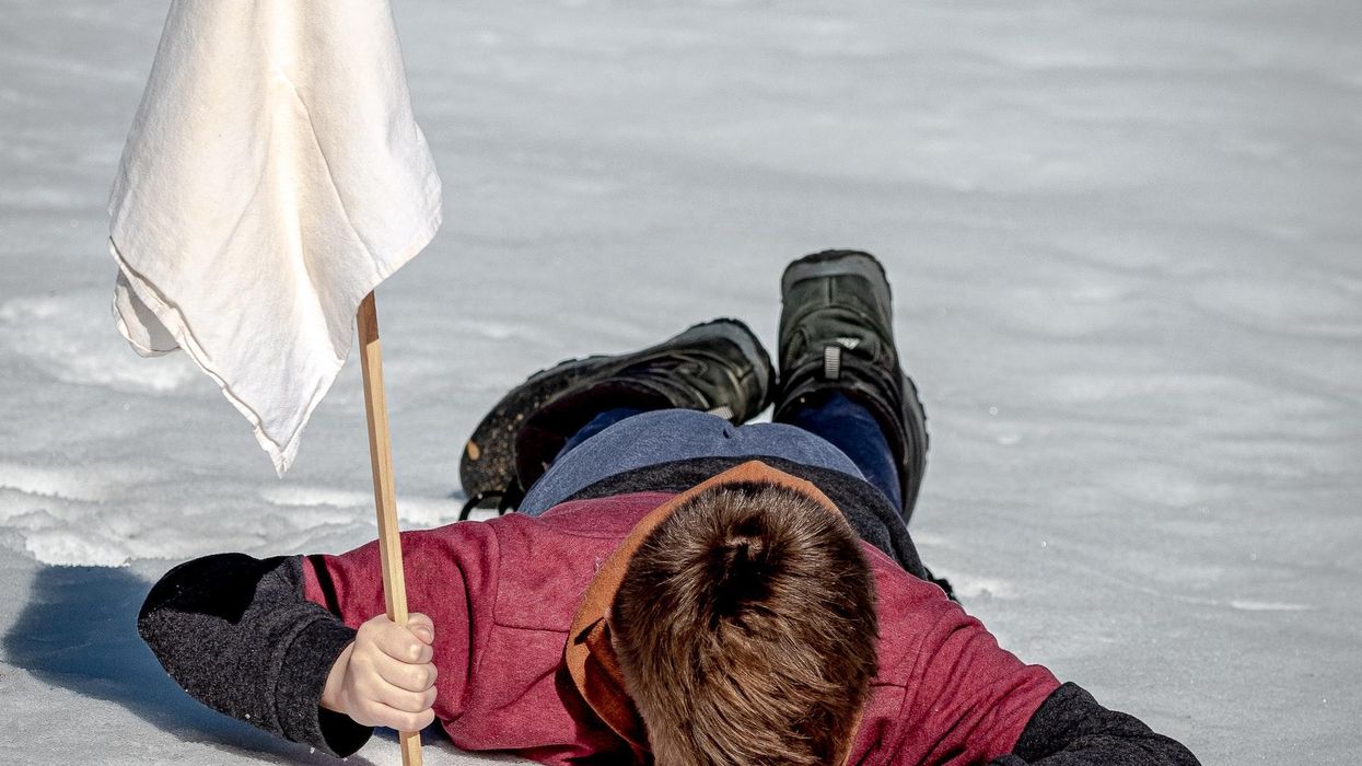 A young man lays face down on ice holding a white flag