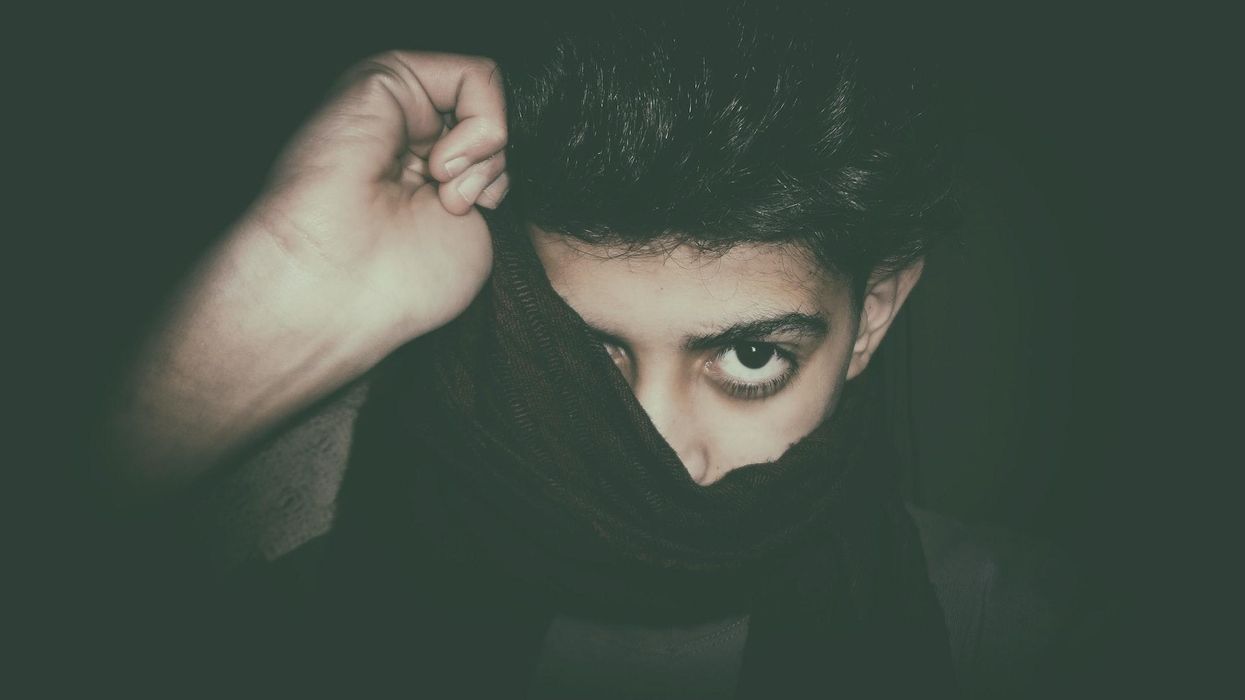 A young man pulls a scarf over his head, hiding one eye