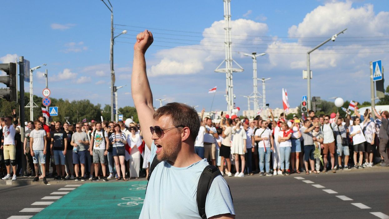 A young man stands and celebrates with his arm in the air in front of a crowd of on-lookers.