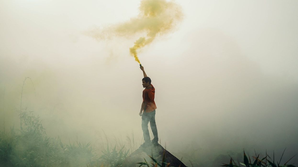 A young man stands on a hill and waves a smoke signal