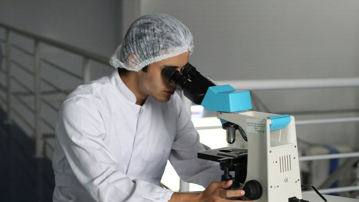 A young scientist looking at a specimen through a microscope on a table.