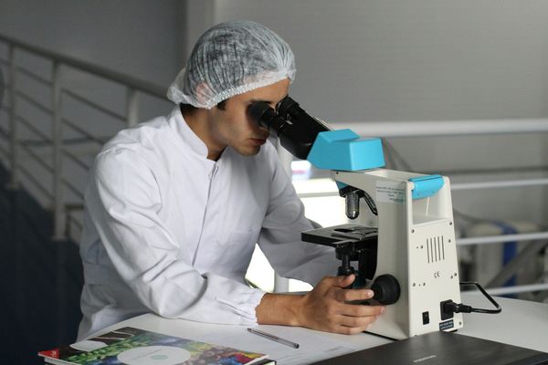 A young scientist looking at a specimen through a microscope on a table.
