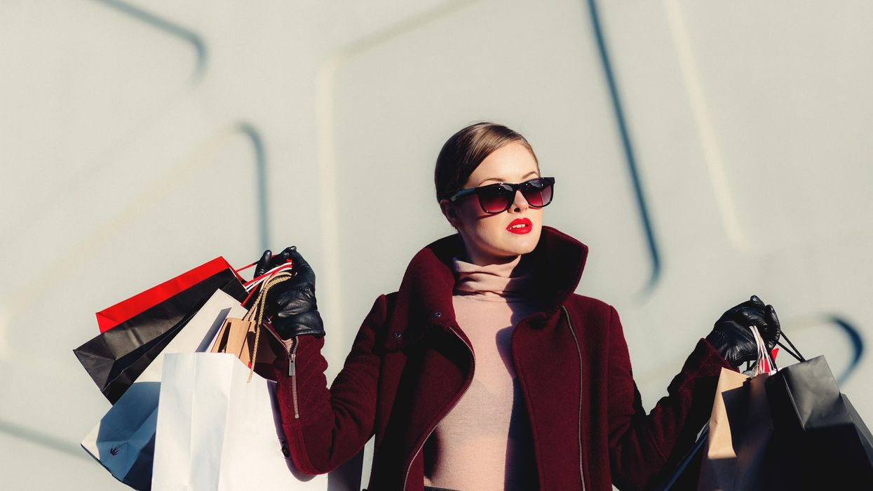 A young woman dressed in high fashion attire, carries tons of shopping bags