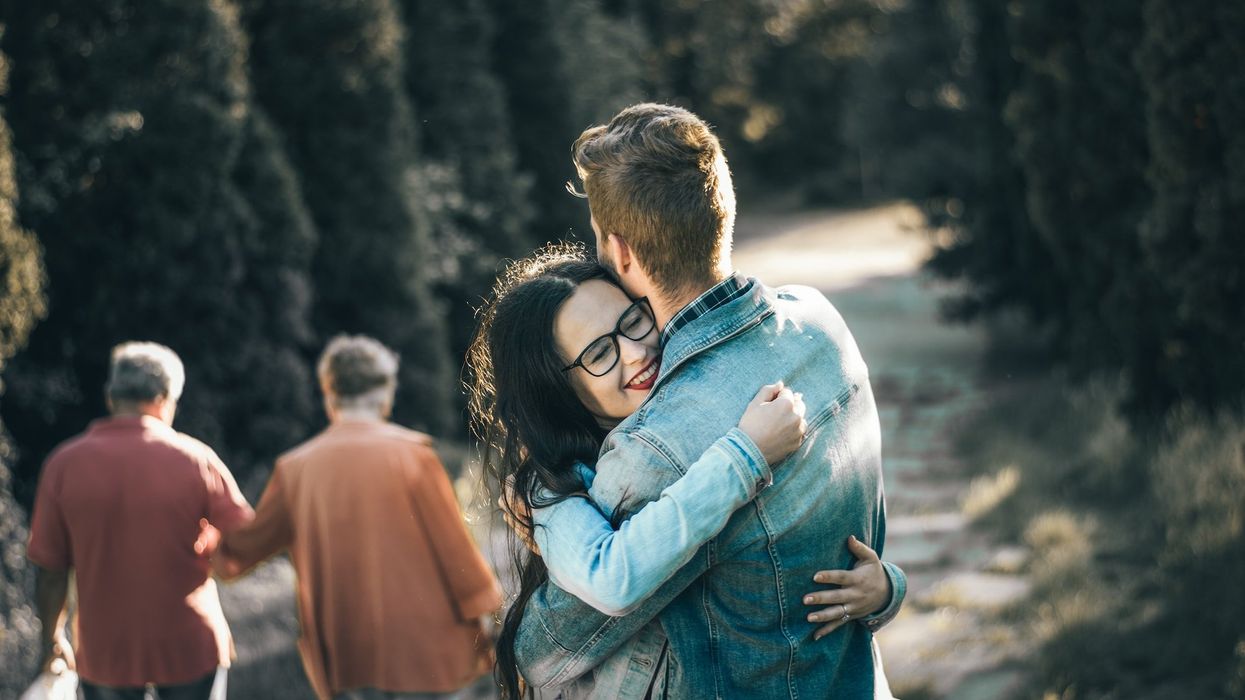 A young woman hugs a young man on a nature trail, as an older couple walks away