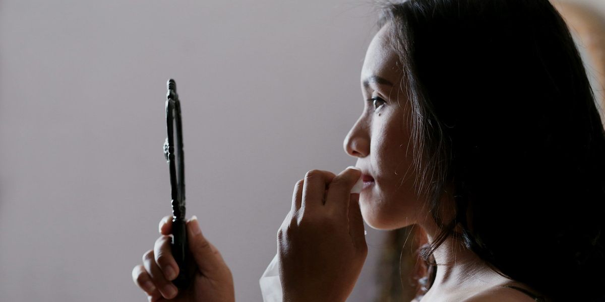 A young woman looks into a hand mirror while she wipes her mouth with a napkin.