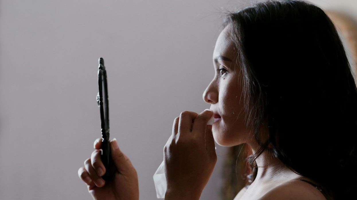 A young woman looks into a hand mirror while she wipes her mouth with a napkin.