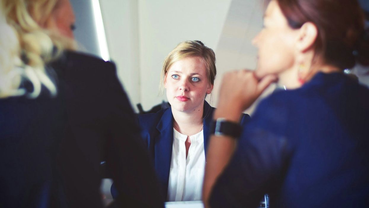 A young woman sits listening to an awkward conversation between two other women