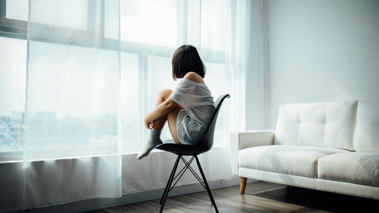 A young woman sitting on a chair, looking out a window