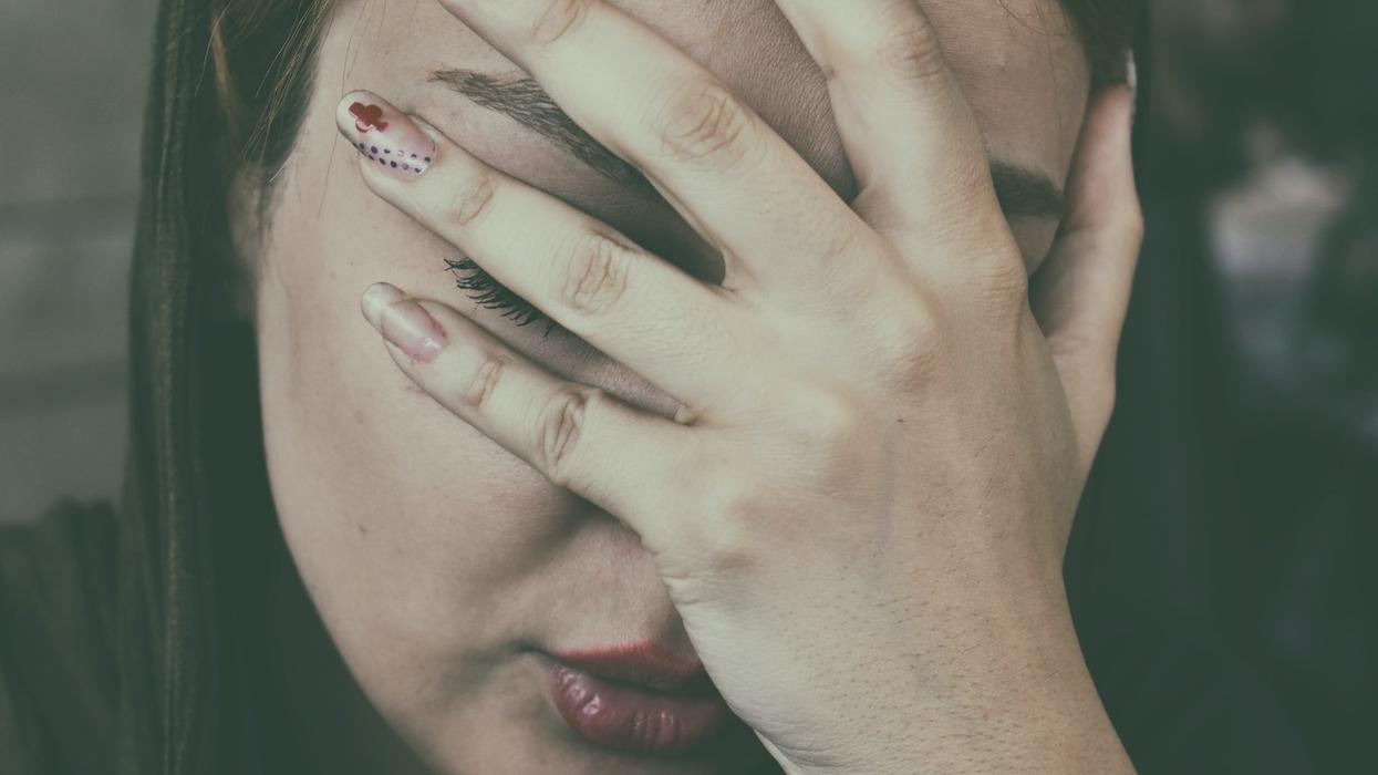 A young woman solemnly holds her face in her hand