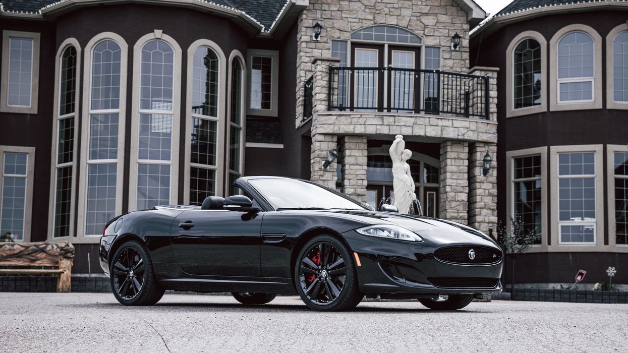 An expensive car sits in front of fabulous, expensive house with a statue