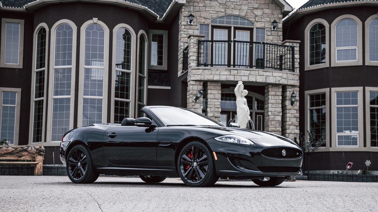 An expensive car sits in front of fabulous, expensive house with a statue