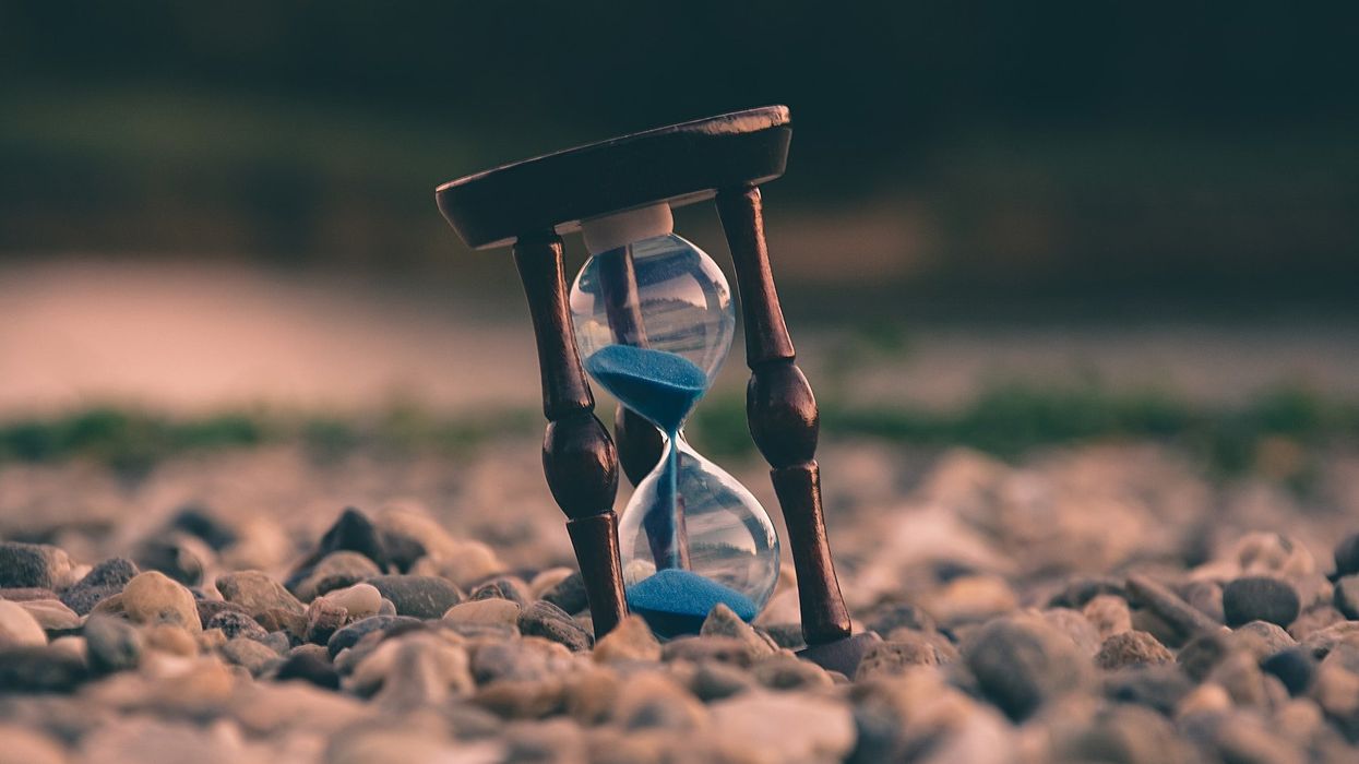 An hourglass with blue sand sits among a field of rocks
