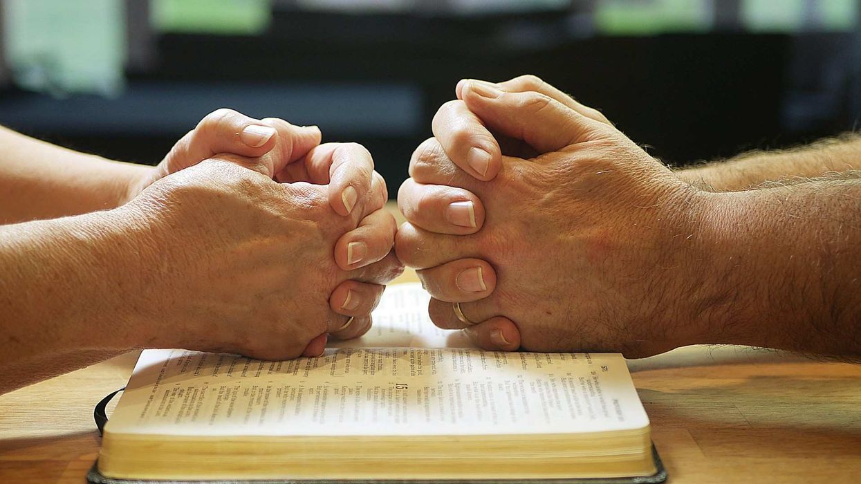 An opposing two sets of hands rest on an open Bible.