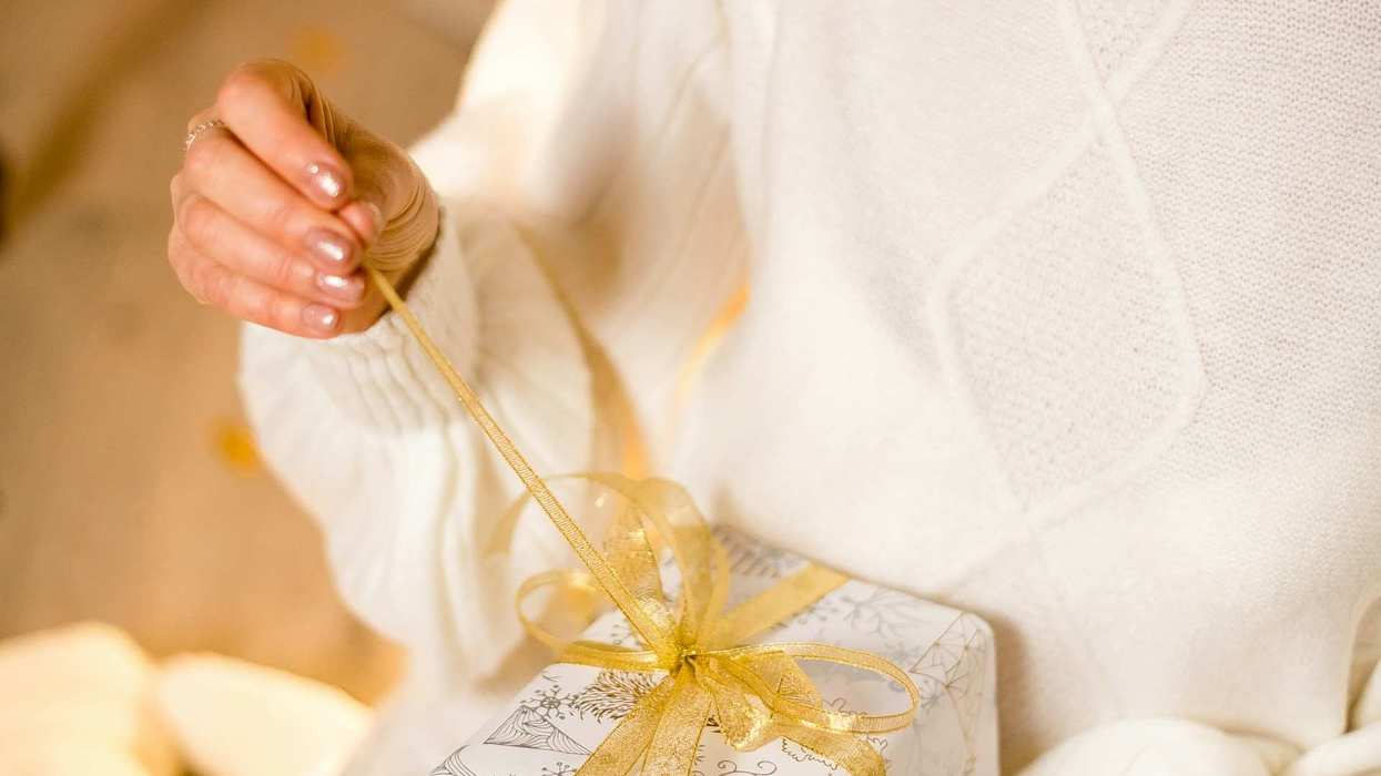 An unidentifiable woman, dressed in all white opens a gift.