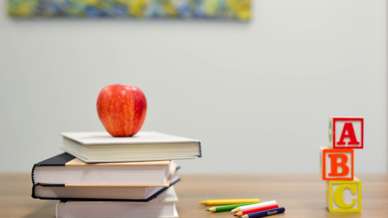 Apple sitting on top of a pile of books, next to colored pencils and ABC blocks.