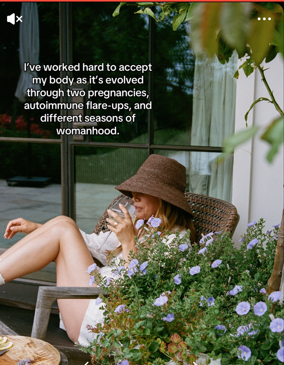Ashley Tisdale sitting in a deck chair behind a bush drinking from a glass.