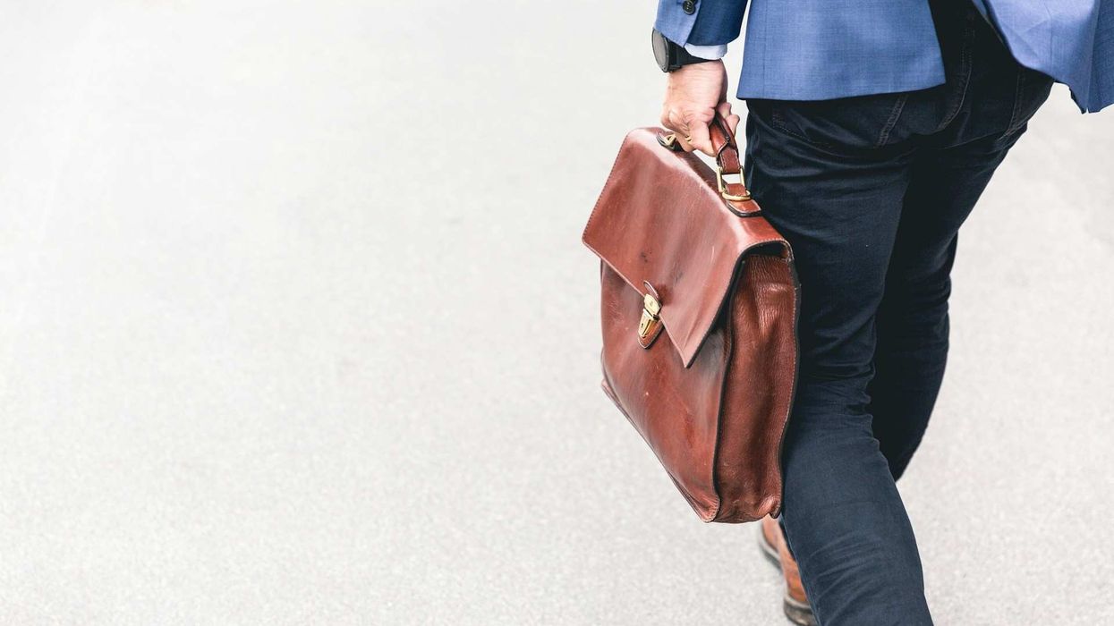 Back shot of a business man walking away. He carries a casual briefcase against a white background.