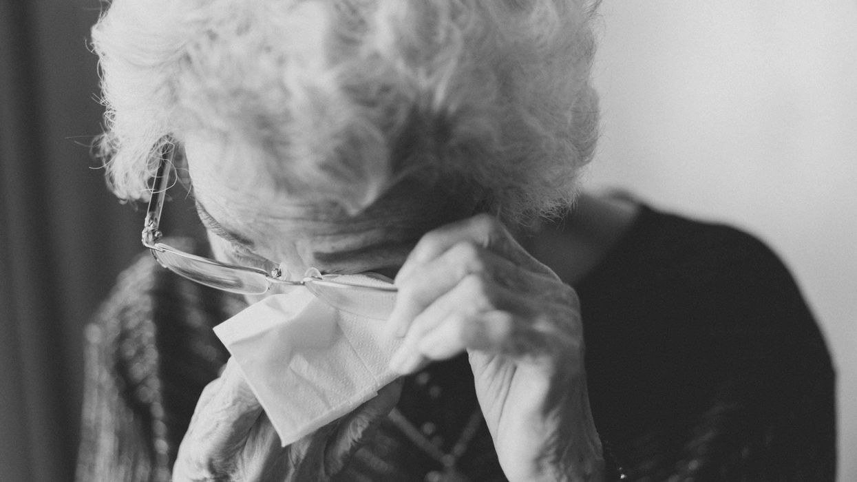 Black and white photo. An elderly woman is wiping her tears with a tissue.