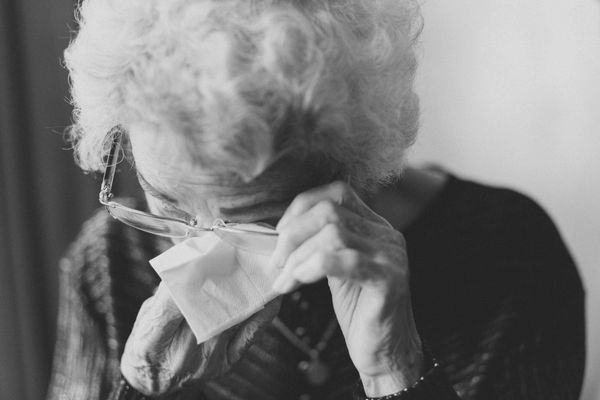 Black and white photo. An elderly woman is wiping her tears with a tissue.