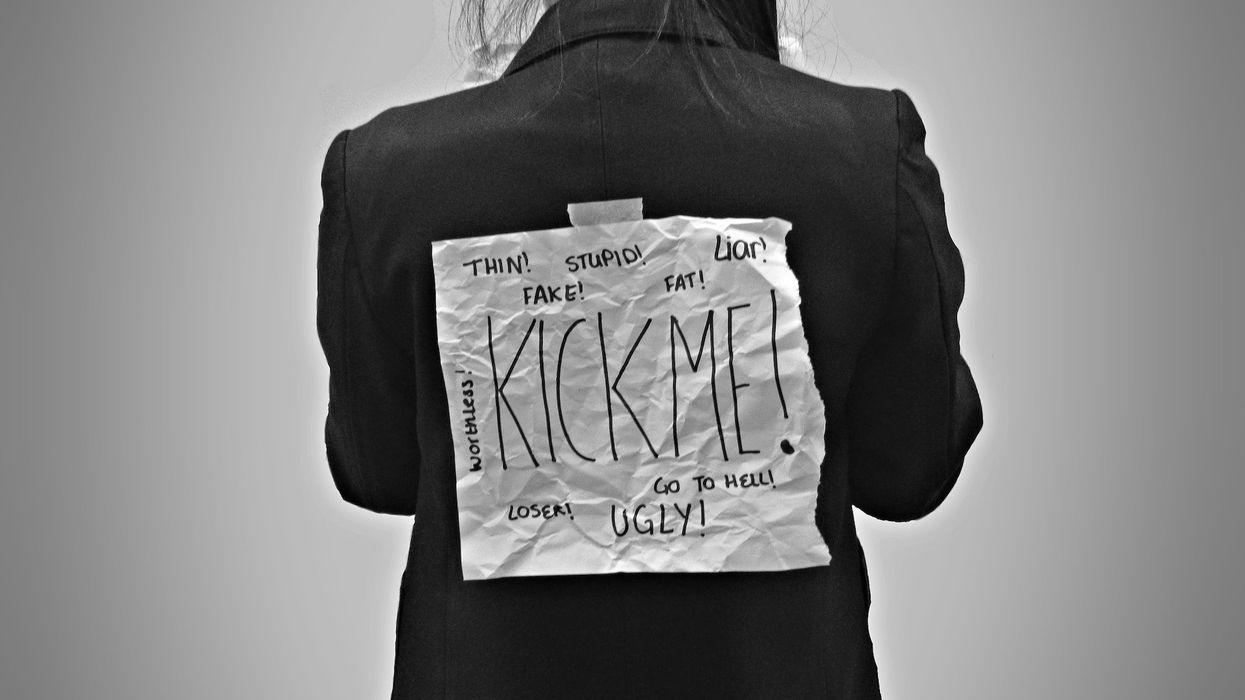 Black and white photo of a girl with a kick me sign, littered with expletives taped to her back