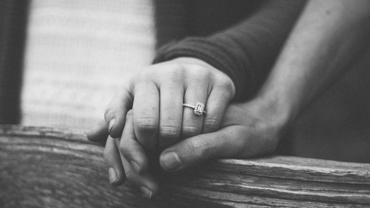 Black and white photo of a woman grasping a man's hand. Her diamond engagement is prominent.