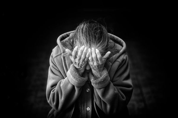 Black and white photo of an elderly person holding their face in their hands